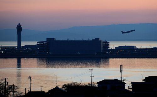 Silhouette city by sea against sky during sunset