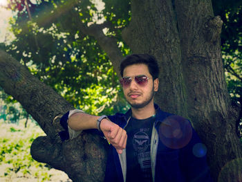 Young man wearing sunglasses while standing by tree trunk in forest