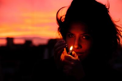 Close-up portrait of young woman burning lighter during sunset