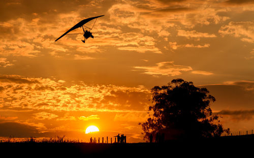 Low angle view of silhouette person hang-gliding against dramatic sky during sunset