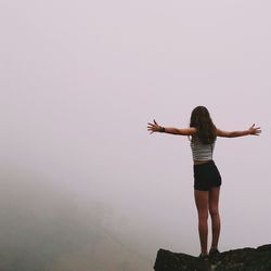 Rear view of young woman standing on cliff during foggy weather