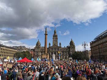 People in front of buildings against cloudy sky