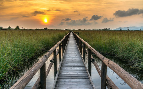 Boardwalk on field against sky during sunset