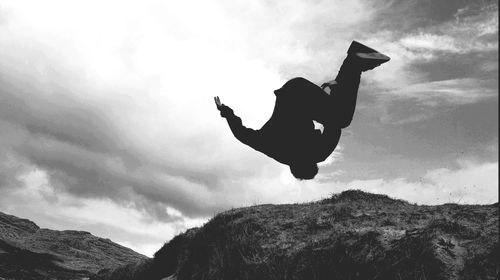 Low angle view of silhouette man jumping against cloudy sky