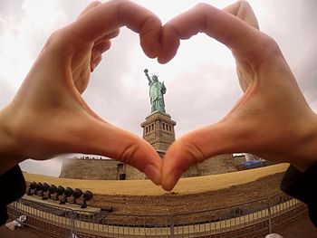 Cropped hand of woman making heart shape against historic statute