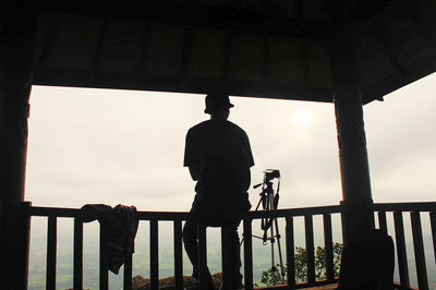 Rear view of silhouette man standing on railing against sky