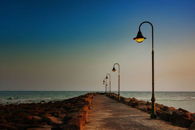 Street light by sea against sky during sunset