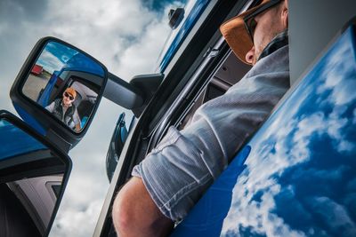 Low angle view of mid adult man reflecting on side-view mirror while sitting traveling in truck