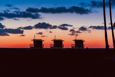 Silhouette hut on beach against sky during sunset