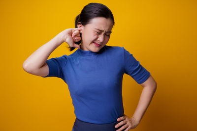 Mid adult woman standing against yellow background