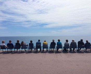 People sitting on chairs by sea against sky