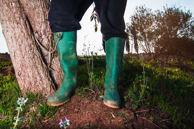 Low section of person wearing green rubber boots while standing on field