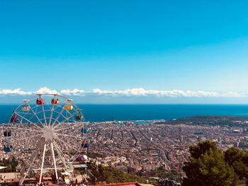 Ferris wheel by sea against blue sky