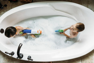 Overhead view of brothers playing with squirt gun in bathtub