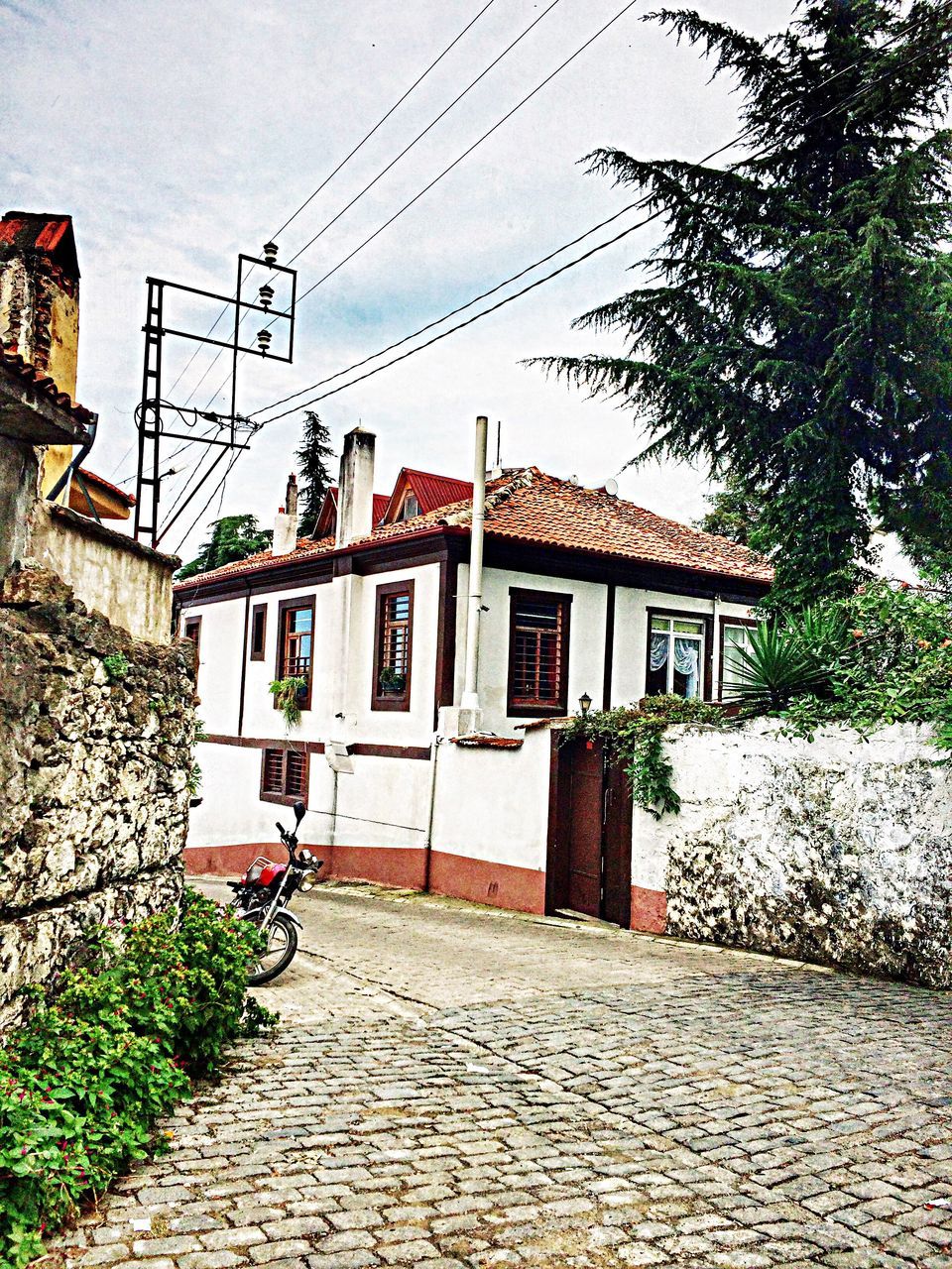 building exterior, architecture, built structure, the way forward, power line, house, street, transportation, residential structure, residential building, cobblestone, diminishing perspective, road, plant, electricity pylon, day, cable, vanishing point, narrow, sky