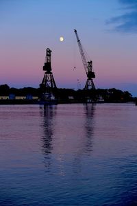 Silhouette cranes against sky at sunset