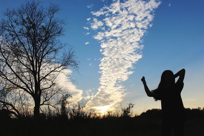 Rear view of silhouette woman standing on field against sky during sunset
