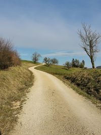 Dirt road amidst field against sky