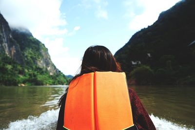 Rear view of woman wearing life jacket in lake against sky