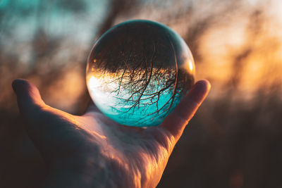 Close-up of hand holding crystal ball against sky