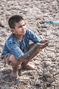 Boy with dirty hands under tap on drought land