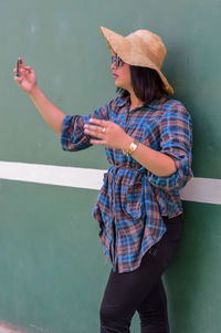 Midsection of woman wearing hat standing against wall