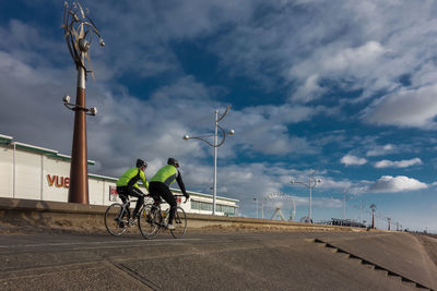 Rear view of men cycling on road against sky