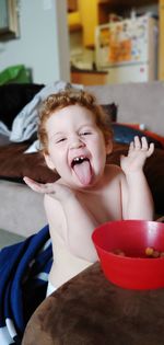 Portrait of shirtless boy sticking out tongue at home