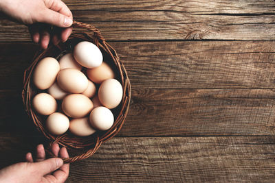 High angle view of person hand holding basked with pasture raised eggs on wooden table background
