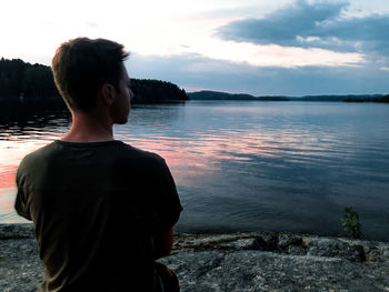 Rear view of man looking at lake against sky