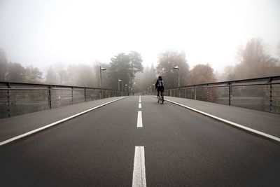 Rear view of man riding bicycle on bridge during foggy weather