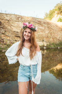 Portrait of smiling young woman standing against waterfall