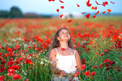 Pretty little girl wearing white dress in summer blooming poppy field playing under evening sun