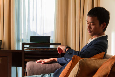 Side view of young woman using mobile phone while sitting at home