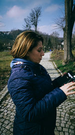 Side view of young woman standing against trees