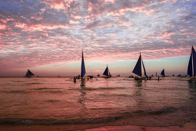 Sailboats sailing on sea against sky during sunset
