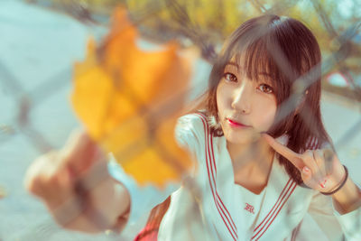 Portrait of young woman standing behind chainlink fence during autumn