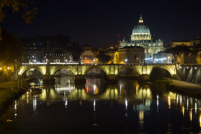 Illuminated bridge over river against buildings in city at night