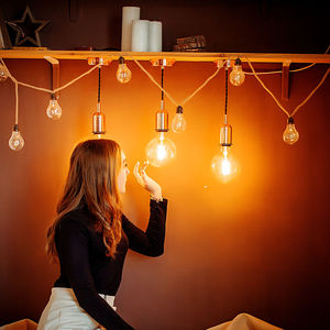 Young woman touching light bulb against wall