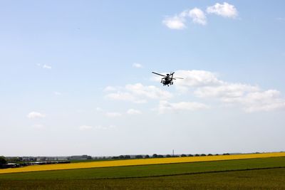 Scenic view of agricultural field against sky with helicopter 