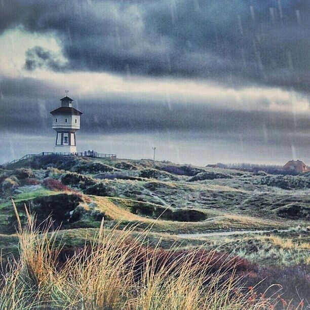 sky, cloud - sky, building exterior, cloudy, lighthouse, architecture, built structure, weather, cloud, guidance, sea, protection, field, storm cloud, overcast, nature, landscape, safety, security, horizon over water