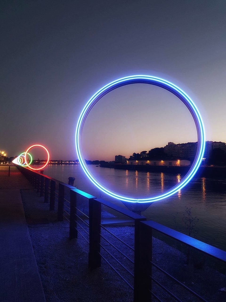 illuminated, night, railing, water, architecture, dark, sky, bridge - man made structure, river, outdoors, diminishing perspective, promenade, engineering, bridge, curve, the way forward, suspension bridge, light painting, spire, ocean