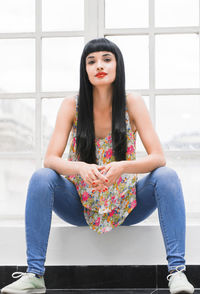 Portrait of beautiful young woman sitting against wall