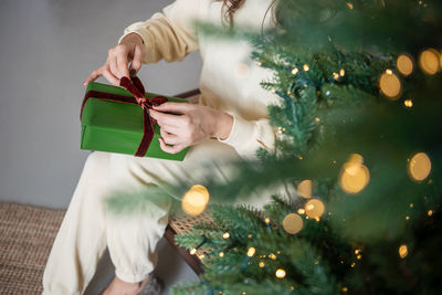 The girl's hands unpack a green gift near the christmas tree