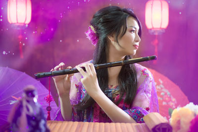 Smiling young woman with flute against illuminated background