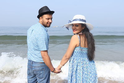 Portrait of smiling couple standing at beach against clear sky