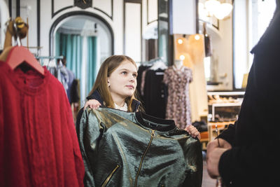 Cute daughter buying fashionable jacket while shopping with father in clothing store