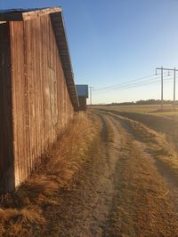 Dirt road amidst field against clear sky