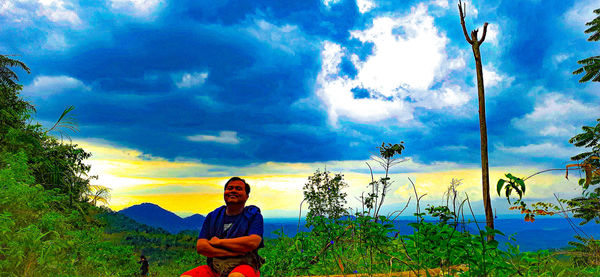 Portrait of young man sitting on land against sky