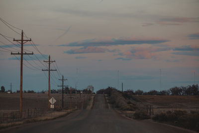 Road by electricity pylons against sky